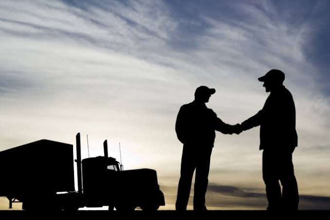 Silhouettes of two men shaking hands beside a semi truck at dusk