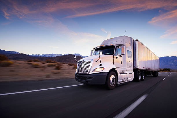 A white semi truck with a trailer driving down an open highway at dusk